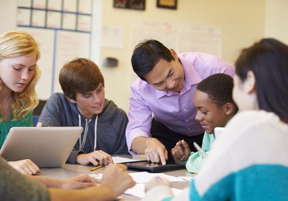 Un professeur de secondaire pointant sur une tablette numérique avec un groupe d'élèves qui la regardent.
